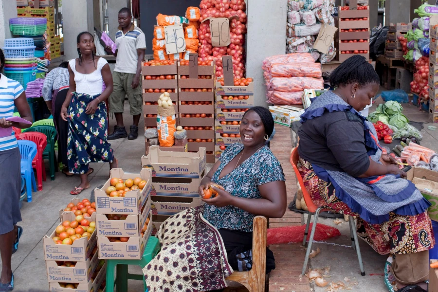 Women traders at a cross-border market, seated among crates of tomatoes, onions and produce laid out for sale
